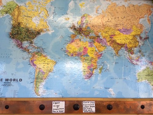 A world map with colorful pins marking various locations, accompanied by a sign about the pins' significance.