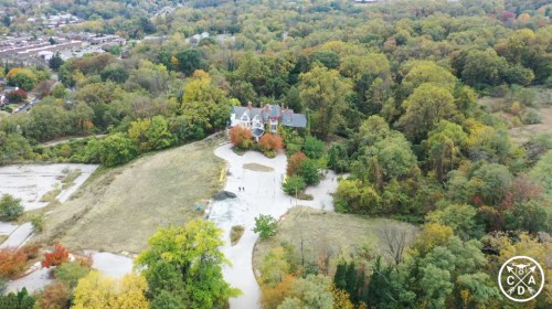 Aerial view of a large house surrounded by colorful autumn trees and an open field.
