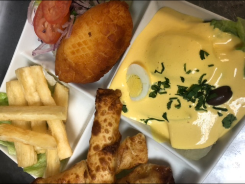 A plate of food featuring a yellow sauce dish, fried snacks, fries, a stuffed pastry, and fresh vegetables.