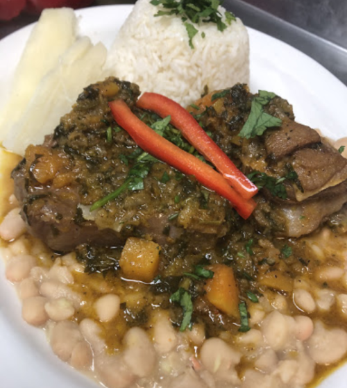 A plate of rice with stewed meat, beans, and garnished with red pepper and herbs, served with plantains on the side.