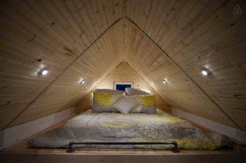 Cozy loft bedroom with a sloped wooden ceiling, featuring a bed with decorative pillows and soft lighting.