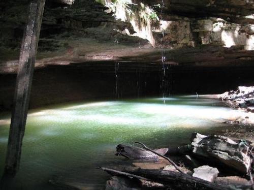 A serene underground pool with clear water, surrounded by rocky walls and faint light filtering through.