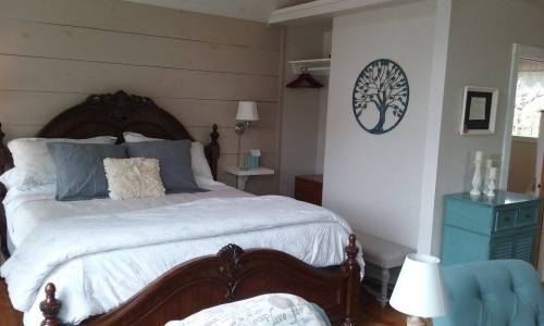 Cozy bedroom featuring a wooden bed, light-colored walls, and a decorative tree wall art.