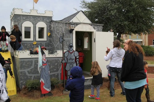 Children play around a castle-themed structure with a knight and princess cutouts, while light snow falls.