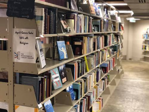 Bookshelves filled with various books on religion, with a sign for an April genre sale offering 50% off.