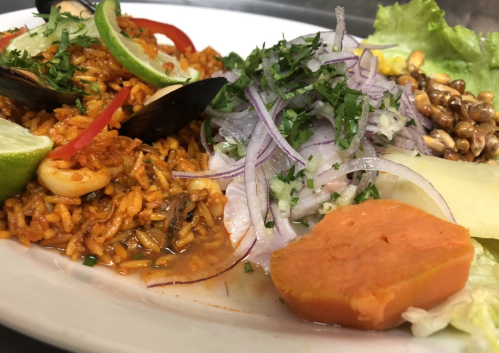 A plate of flavorful rice with seafood, garnished with lime, onions, lettuce, and a side of sweet potato.