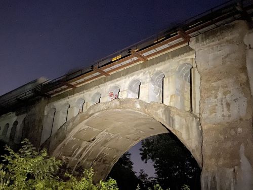 A dimly lit stone bridge with arches, partially covered in graffiti, set against a night sky.