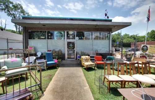 A storefront with a variety of vintage furniture displayed outside on a sunny day.