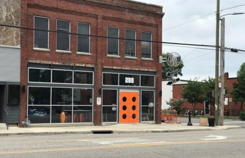 A brick building with large windows and an orange door, featuring the number 200, on a quiet street.