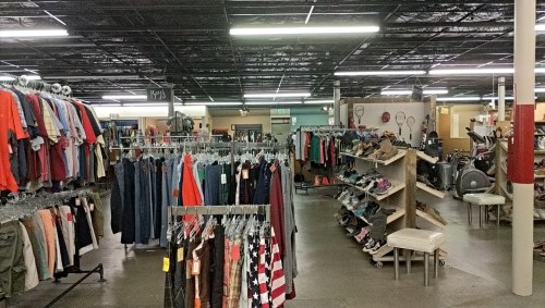 A spacious thrift store interior with racks of clothing, shoes, and various items displayed on shelves.