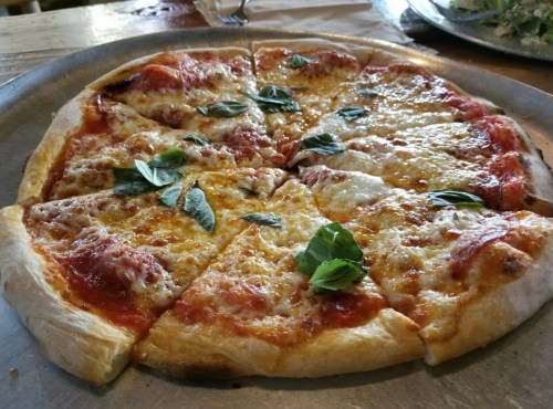A freshly baked pizza with melted cheese, tomato sauce, and fresh basil leaves, sliced into eight pieces.