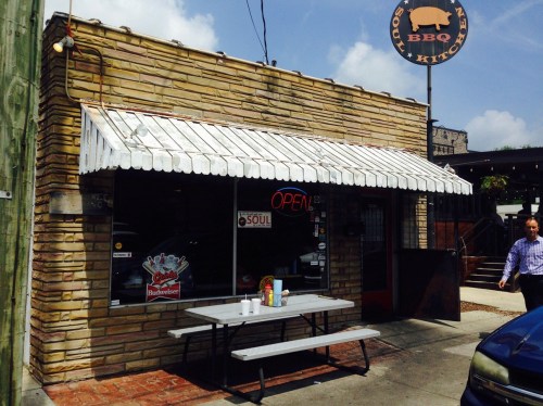 A small BBQ restaurant with a stone exterior, open sign, and outdoor seating under a striped awning.