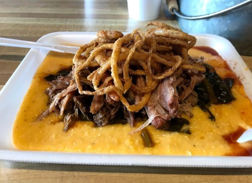 A plate of pulled pork topped with crispy onions, served over greens and a creamy sauce.