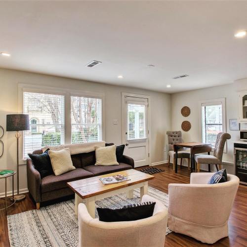 Cozy living room with a sofa, armchairs, coffee table, and dining area, featuring large windows and warm wood flooring.