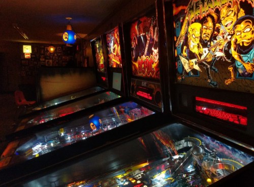 A dimly lit arcade with colorful pinball machines featuring vibrant artwork and glowing lights.