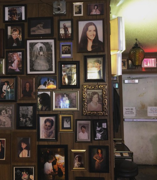 A wall covered in various framed photographs, featuring portraits of people in different styles and settings.