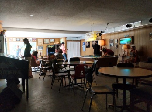 A casual gathering in a dimly lit room with people playing games and socializing around tables and a pool table.