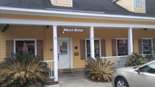 Exterior of a yellow building with a sign reading "MEAT BOSS" and an "OPEN" sign in the window.