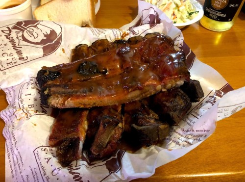 A plate of barbecue ribs glazed with sauce, served with bread and coleslaw on the side.