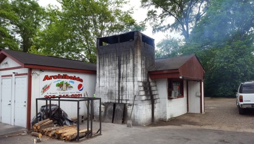 A building with a charred chimney, surrounded by trees, and a sign for "Archibaldo's" visible on the wall.