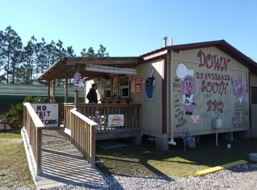 A colorful BBQ restaurant with a wooden deck, featuring pig-themed decor and a sign that says "Open."
