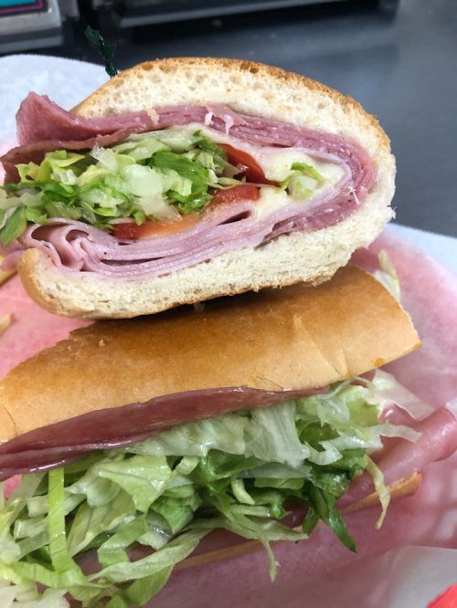 A close-up of a sandwich with layers of deli meats, lettuce, and tomato, cut in half and stacked on a plate.