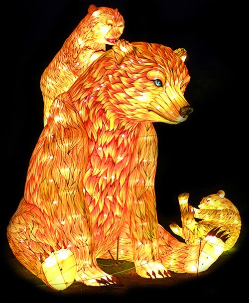 A vibrant lantern display featuring three bears, showcasing intricate designs and warm colors against a dark background.