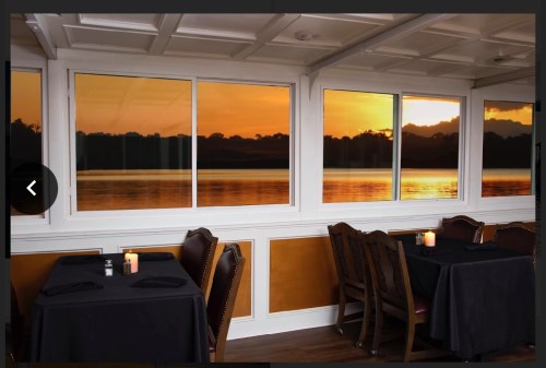 Cozy restaurant interior with candlelit tables, featuring large windows showcasing a sunset over the water.