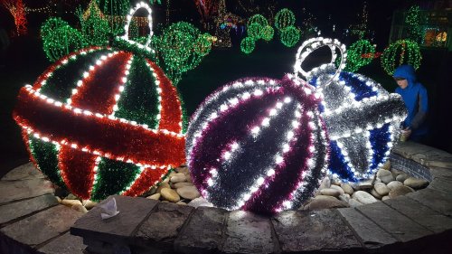 Colorful illuminated ornaments in red, green, and silver, surrounded by stones, with festive lights in the background.