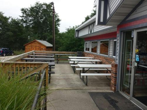 Outdoor seating area with picnic tables beside a building, surrounded by greenery and a wooden shed in the background.