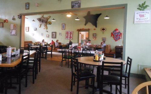 A cozy restaurant interior with wooden tables, chairs, and decor, featuring patrons dining and chatting in a relaxed atmosphere.