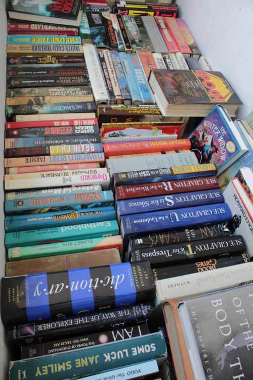 A variety of books stacked in a box, featuring colorful covers and diverse genres.
