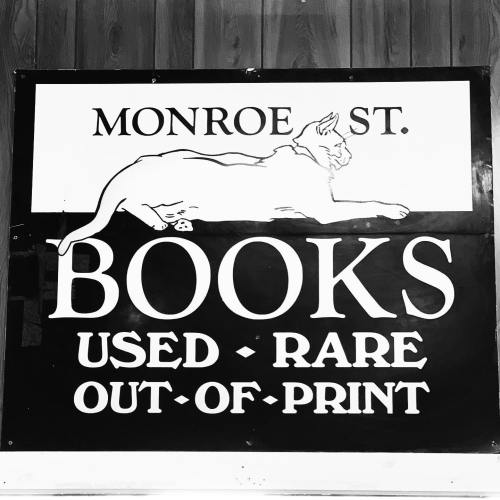Sign for Monroe St. Books featuring a cat illustration, advertising used, rare, and out-of-print books.
