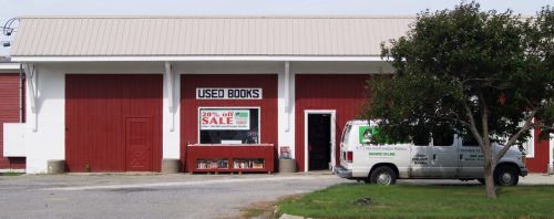 A storefront with a sign reading "USED BOOKS" and a sale banner, featuring a van parked nearby.