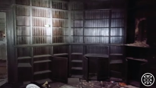 Dimly lit room with dark wooden shelves, some empty, and debris scattered on the floor.