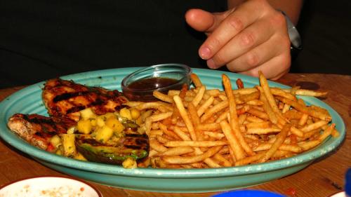 A plate of grilled chicken with mango salsa and a side of crispy fries, with a hand reaching for the food.