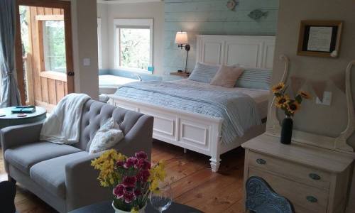 Cozy bedroom with a white bed, blue accents, and a sitting area featuring a gray sofa and flowers on a table.