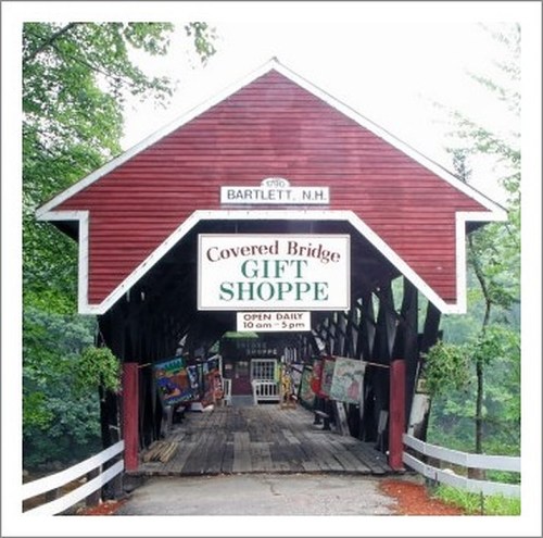 A red covered bridge with a sign for a gift shop, surrounded by greenery in Bartlett, New Hampshire.