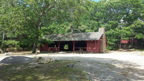 A rustic red cabin surrounded by trees, with a stone chimney and a gravel path in front.