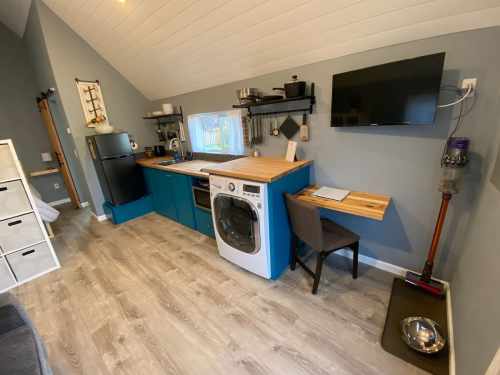 A compact kitchen with blue cabinets, a washer, and a TV, featuring a wooden countertop and a small dining area.