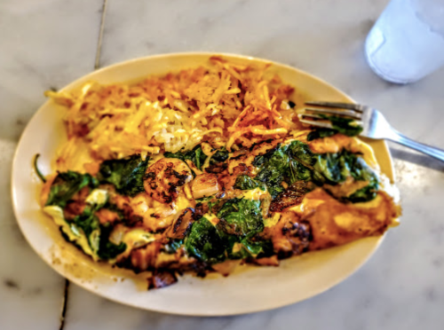 A plate of spinach and cheese omelette with hash browns on the side, served on a white dish.