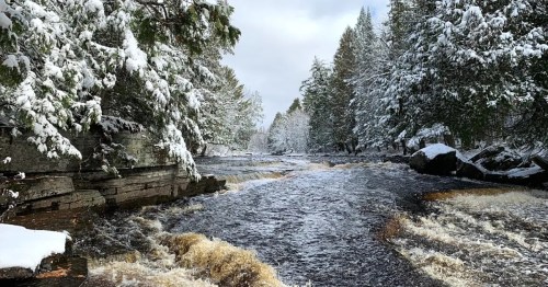 A snowy river scene with frosted trees lining the banks and flowing water, creating a serene winter landscape.