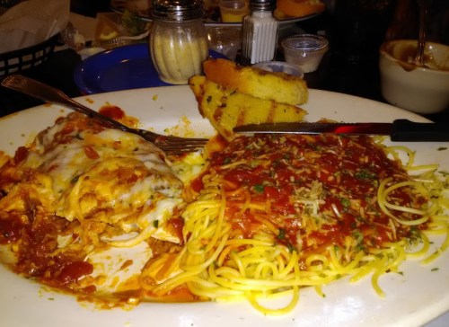 A plate of cheesy chicken enchiladas and spaghetti with marinara sauce, accompanied by a slice of garlic bread.