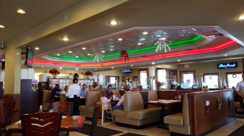 A cozy restaurant interior with festive red and green lighting, booths, and diners enjoying their meals.