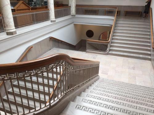 A spacious staircase with wooden railings and marble steps, leading to an upper level in a well-lit building.