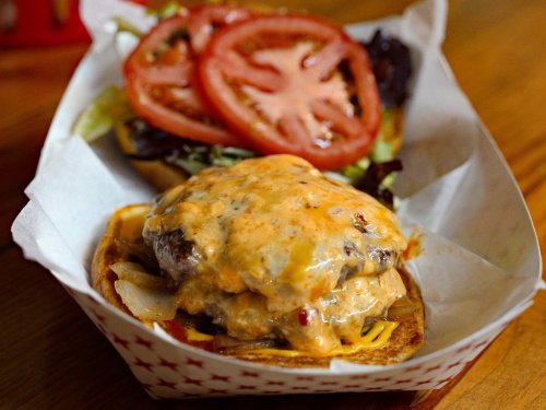 A close-up of a cheeseburger with melted cheese, onions, lettuce, and tomato in a paper-lined basket.