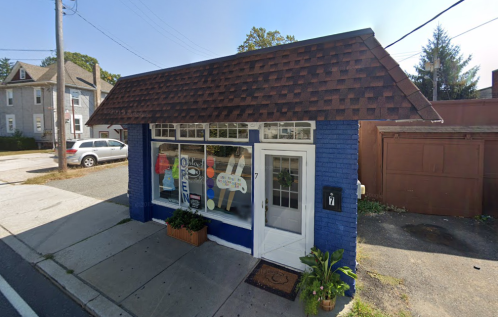 A small blue building with a brown shingled roof, featuring large windows and an "OPEN" sign.