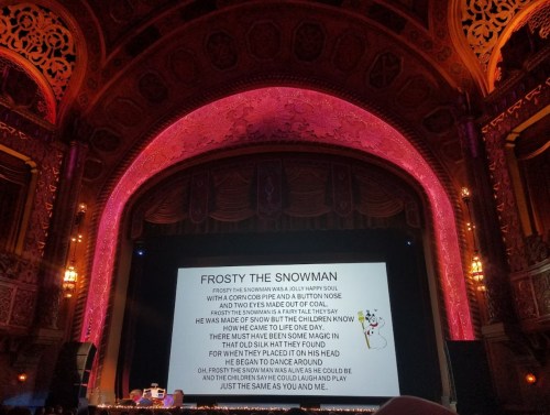 A stage with a colorful backdrop and lyrics for "Frosty the Snowman" displayed on a screen.