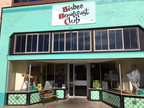 Exterior of the Bisbee Breakfast Club, featuring a turquoise facade, large windows, and a welcoming "OPEN" sign.