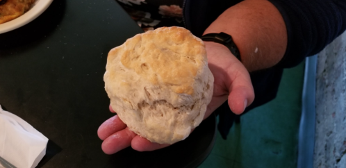 A person holding a large, fluffy biscuit in their hand, showcasing its golden-brown top and soft texture.